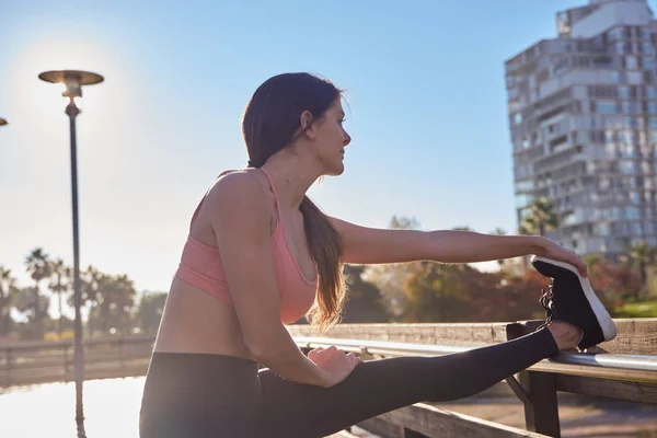 Young woman raises her leg and stretches her arm — Stock Photo, Image