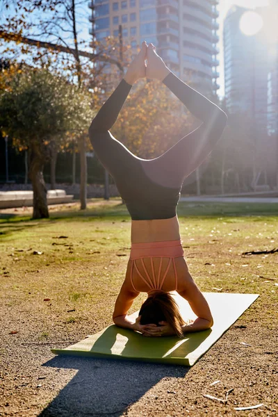 Woman does a yoga lotus head stand in the park