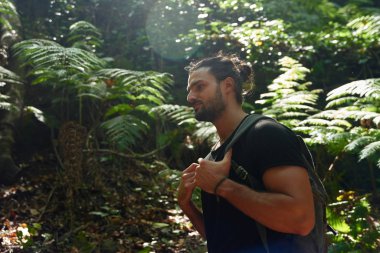 Genç sakallı adam ormanda yürüyor.