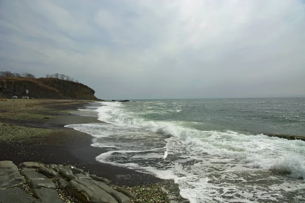 Hermosa playa desierta, olas y bryzni en las rocas, vidrio liso — Foto de Stock