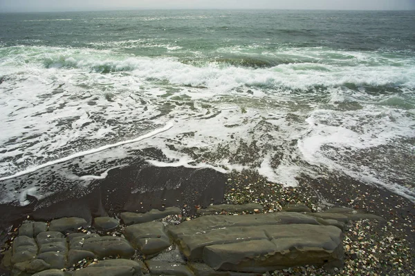 Vacker öde strand, vågor och bryzni på klipporna, släta glas — Stockfoto