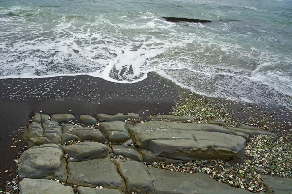 Hermosa playa desierta, olas y bryzni en las rocas, vidrio liso — Foto de Stock