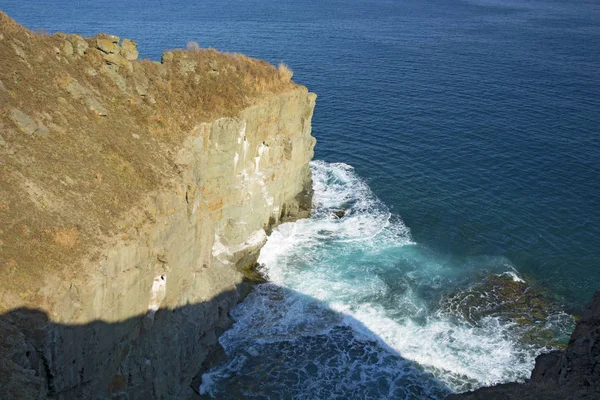Alto acantilado sobre el mar, el acantilado desciende al mar, muchas salpicaduras de olas y piedras — Foto de Stock