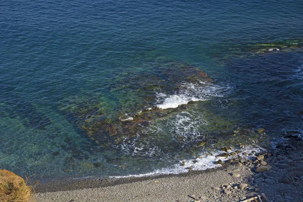 Hög klippa ovanför havet, klippan sjunker ner i havet, många stänkande vågor och sten — Stockfoto