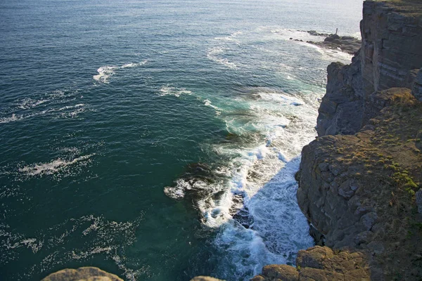 High cliff above the sea, the cliff descends into the sea, many splashing waves and stones — Stock Photo, Image