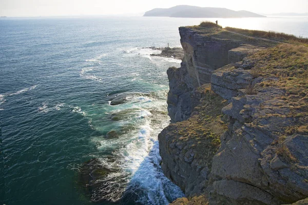 High cliff above the sea, the cliff descends into the sea, many splashing waves and stones — Stock Photo, Image