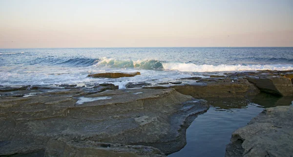 Hög klippa ovanför havet, klippan sjunker ner i havet, många stänkande vågor och stenar — Stockfoto