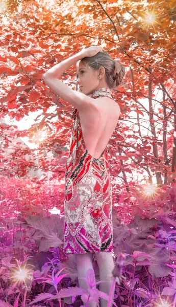 Uma menina em um vestido com costas nuas vale a pena na folhagem na floresta, floresta vermelha. cabelo decorado com folhagem . — Fotografia de Stock