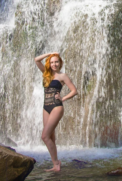 Schöne Mädchen posiert in einem hohen Wasserfall, absolut verlassen rothaarige Mädchen in einem Wasserfall. — Stockfoto