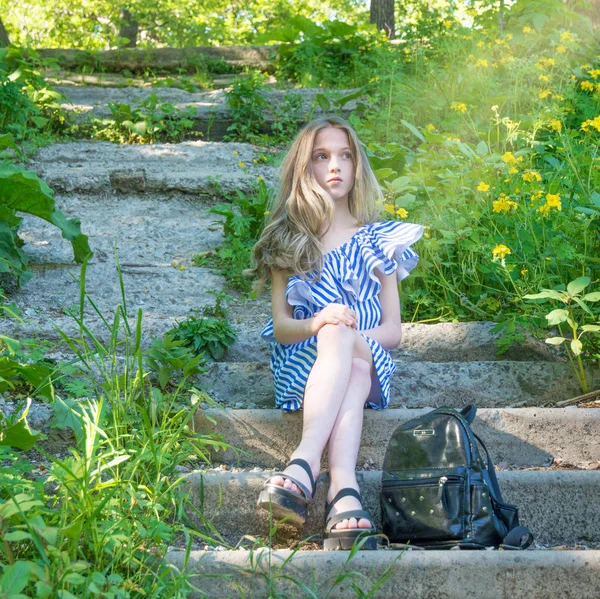 Krásná mladá dívka sedí na schodech v parku s květinou, — Stock fotografie