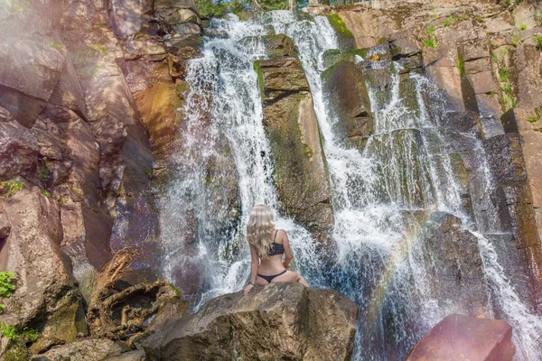 Bela menina magra posando no fundo de uma cachoeira salpicando água e sol brilhante . — Fotografia de Stock