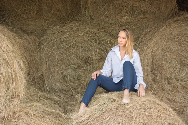 Hermosa joven con una camisa y pantalones sentados en el granero . — Foto de Stock