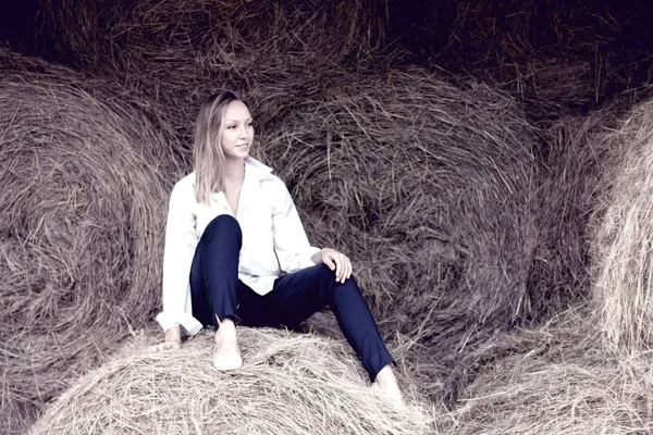Hermosa joven con una camisa y pantalones sentados en el granero . — Foto de Stock