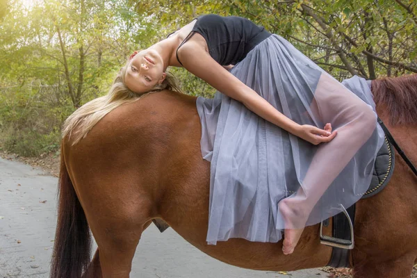 Egy fiatal, szőke lány pózol egy ló, egy gyönyörű lány, és egy erős ló. — Stock Fotó