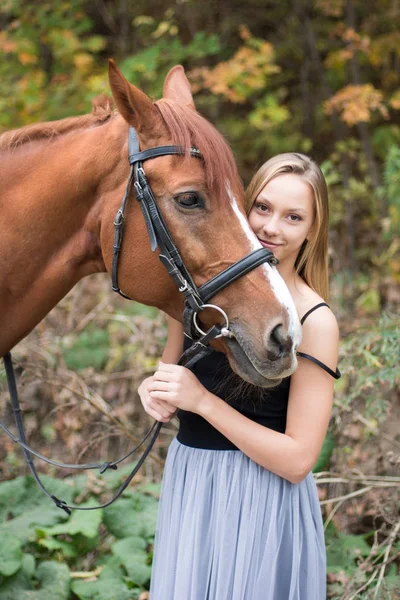 Egy fiatal, szőke lány pózol egy ló, egy gyönyörű lány, és egy erős ló. — Stock Fotó