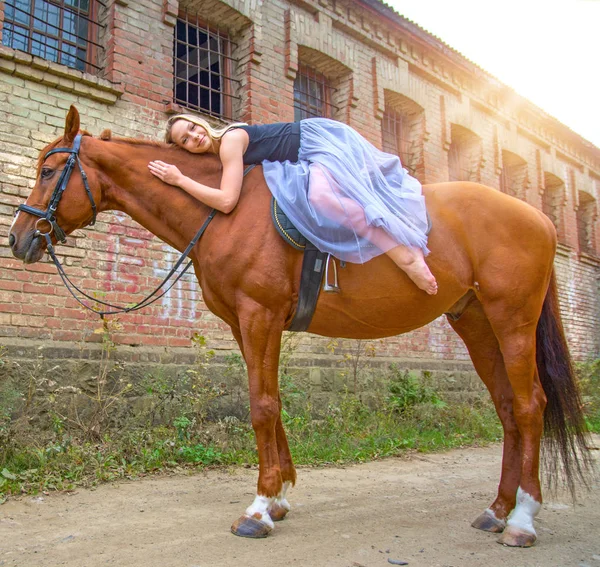 Una joven rubia posando con un caballo, una hermosa chica y un caballo fuerte . — Foto de Stock