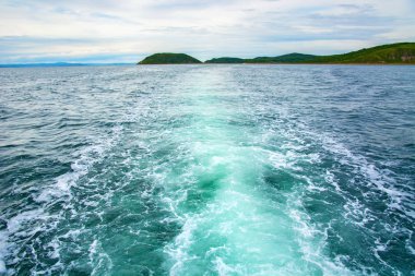 arkasından su ve kabarcıklar güzel bir tüy tekne yüzen ufukta adanın görebilirsiniz. 