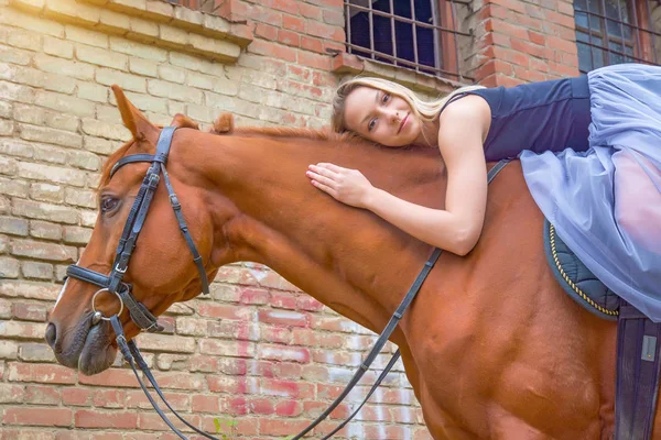 Una joven rubia posando con un caballo, una hermosa chica y un caballo fuerte . — Foto de Stock