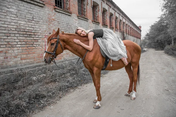 Egy fiatal, szőke lány pózol egy ló, egy gyönyörű lány, és egy erős ló. — Stock Fotó