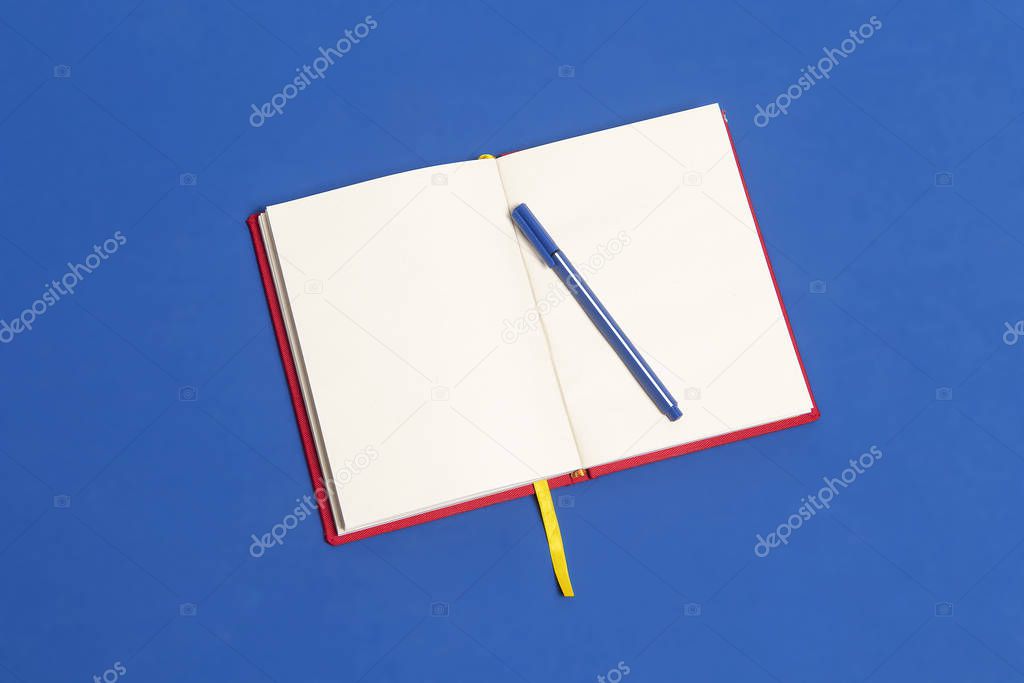 Cuaderno rojo abierto con cinta amarilla de separador sobre una mesa de color azul clsico y lapicero. Colores de la bandera de Colombia