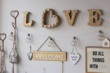 Pared de casa en color blanco con decacin en madera rida, con bombillos, cuadros, corazones y mensajes. Letrero de amor en madera