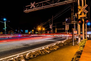 Demiryolu parça geçiş saatinde meşgul bir yolda geçen trafiğine. Tren gece commuters ile geçerken ışık parlamaları ve kapısı araba durdurmak. Uzun pozlama etkisi.