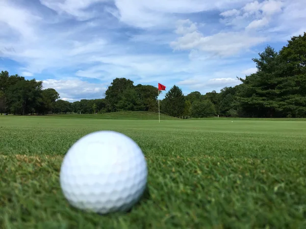 Een witte golfbal zit op de voorgrond vlakbij het groen van een cursus op een mooie herfstdag. Chip of putt sloeg in de beker. — Stockfoto