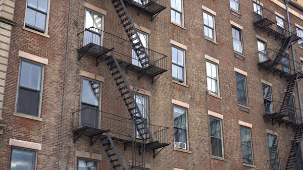 Exterior establishing photo of a New York style apartment building during the day. Windows and steel fire escape hug the brick facade for safety.