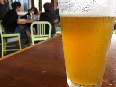 Hafif Lager ile uzun pint buzlu bira cam fotoğraf yakın kadar rahat restoranda ahşap masada oturan döktü. Aile bulanıklık arka planda birlikte yemek seviyor