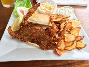 Susam tohumu çörek taze patates cipsi, lahana salatası, tartar sosu ve gurme beyaz tabakta bir sahil restoranı hizmet limon ile lezzetli kızarmış yumuşak Kabuk Yengeç sandviç