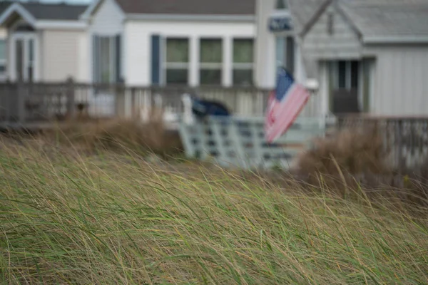 Bandeira americana voar no vento a partir de praia casa profundidade de campo desfoque fundo contra areia duna grama ao longo EUA costa — Fotografia de Stock