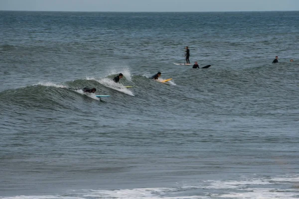 Reihe von Surfern, die am Strand eine große Welle im Meer fangen. schnelle Extremsportbewegungen verschwimmen. — Stockfoto