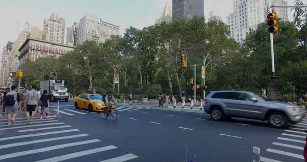 Vue large à l'extérieur du parc de New York de l'intersection animée de Manhattan de voitures passant et de personnes marchant à travers la rue dans un passage piétonnier de sécurité un jour d'été — Photo