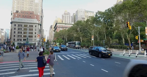 Vue large à l'extérieur du parc de New York de l'intersection animée de Manhattan de voitures passant et de personnes marchant à travers la rue dans un passage piétonnier de sécurité un jour d'été — Photo