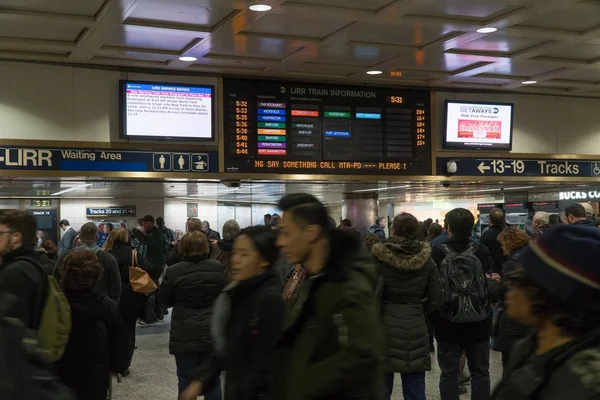 Pasajeros del ferrocarril de Long Island esperan en el vestíbulo bajo un gran cartel de la junta para recibir anuncios de vías de tren que salen de Nueva York y viajan a casa durante la hora punta —  Fotos de Stock