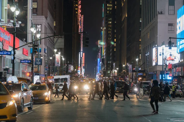 Vista panorámica nocturna del cruce del centro de Manhattan NYC durante la hora punta. La gente camina con seguridad a través de la intersección avenida en el semáforo — Foto de Stock