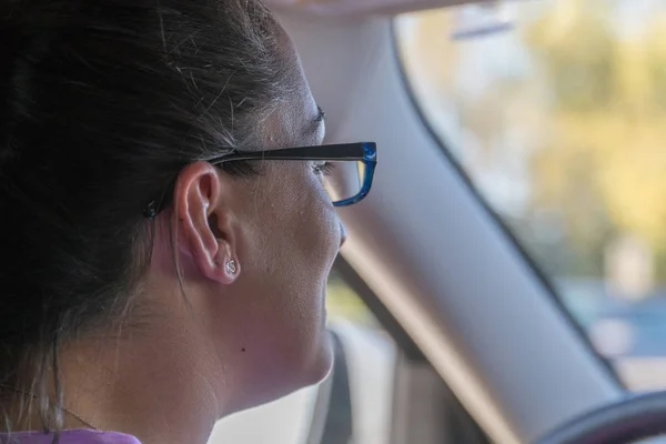 美丽的年轻女子戴着眼镜肩上的视角开着车上路 — 图库照片