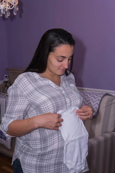 美丽怀孕的新妈妈折叠婴儿连体在她的肚子准备的小女孩回家第一次的托儿所 兴奋的父母为分娩和生活事件 — 图库照片