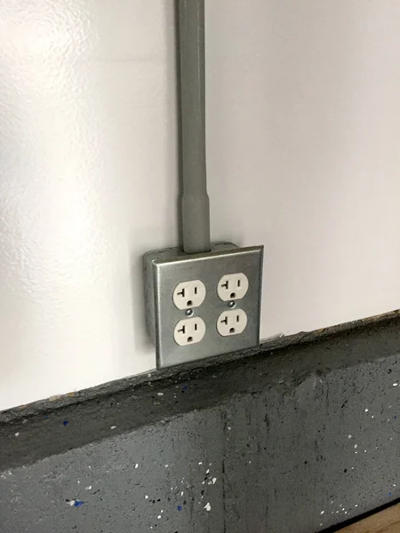 2 gang power outlet receptacle box mounted on a white wall over concrete flooring. Garage workshop type setup. Electrical romex hot neutral and ground copper wire hidden behind PVC plastic pipe