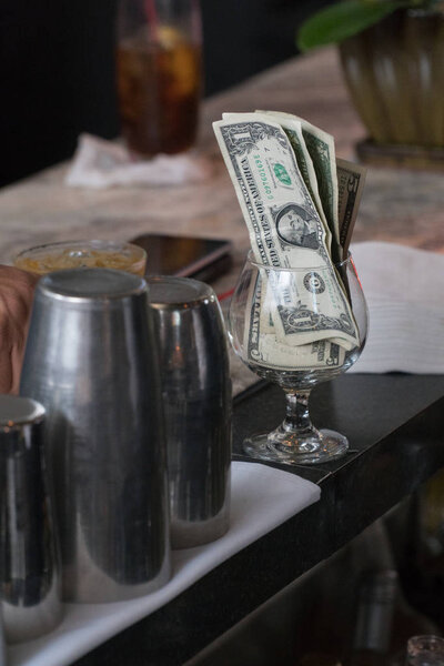 Cash tips in a cocktail glass on bar counter top. Customers give money as thanks for proper service to bartender when ordering and making drinks for patrons at restaurant