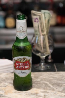 New York, 2018 yaklaşık: Stella Artois bira şişesi üzerinde restoran bar tezgah üstü. Alkol barmen tarafından müşterilere servis. Nakit ödeme ve cam arka planda ipuçları için. Açıklayıcı yazı işleri
