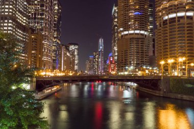 Gece vakti dış görünüş, Chicago nehir cephesine bakan bir çekim. Ufuk çizgisi karanlık gökyüzünde aydınlanıyor. Güzel bir sahnede sudan yansıyor.