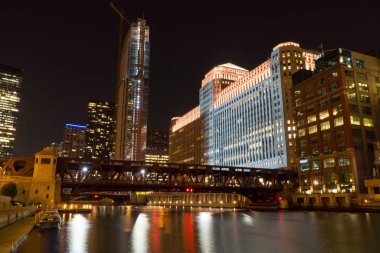 Gece vakti dış görünüş, Chicago nehir cephesine bakan bir çekim. Ufuk çizgisi karanlık gökyüzünde aydınlanıyor. Güzel bir sahnede sudan yansıyor.