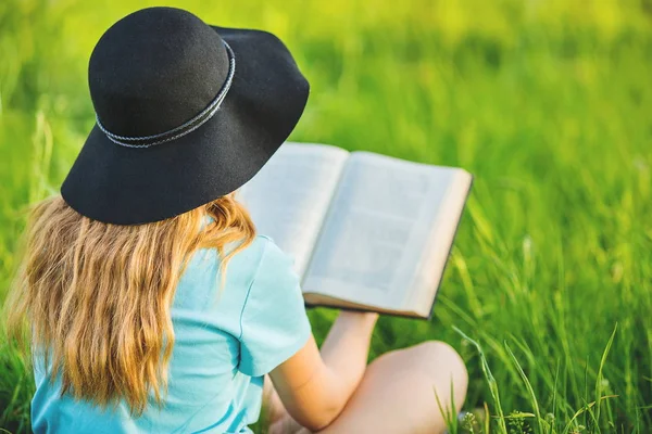 Flickan sitter på en gräs och läser en bok — Stockfoto