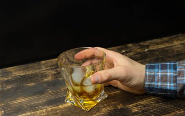 Bardak viski buz küpleri ile boşluk ile rustik ahşap masa üzerinde tutan adamın el