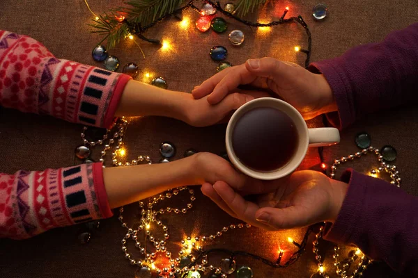 Hands holding mug of coffee. Dark table. Glowing light bulb. Accessories. New year. Christmas. The elements of design.