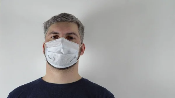 On the face of a man is a medical mask. Portrait of a man. Dark clothes. Virus protection. Precautionary measures. Light background