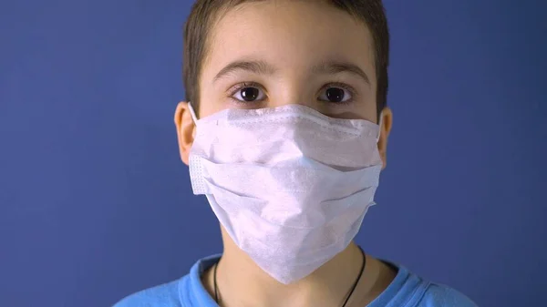 A boy with a medical mask on his face. Dark hair. Age 6 years. Virus protection. Precautionary measures. Light background
