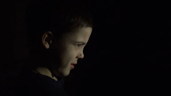 A boy is standing in the dark. Side view. Offended face. Close-up. Punishment. Learning problems.