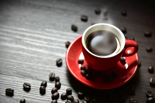 Café de taza roja con humo y grano de café en textura de mesa de madera, enfoque selectivo en el borde de la taza, concepto de bebida, concepto de relajación — Foto de Stock